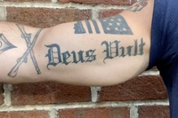 A "Deus Vult" tattoo featuring crossed rifles and an American flag, symbolizing Crusader rhetoric.